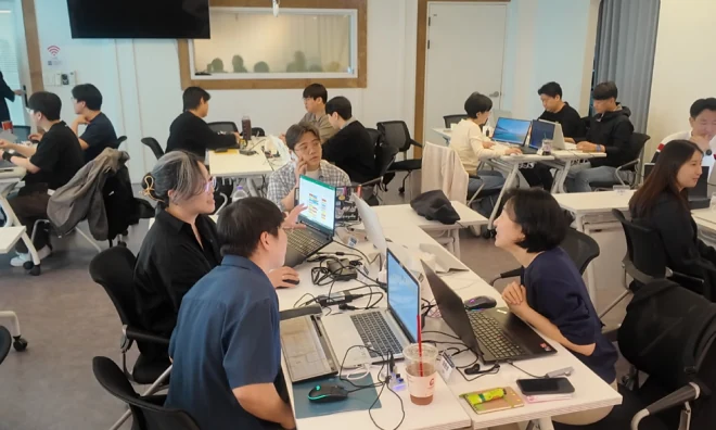 여러 수강생이 테이블에 둘러앉아 각자의 노트북으로 실습하는 강의실